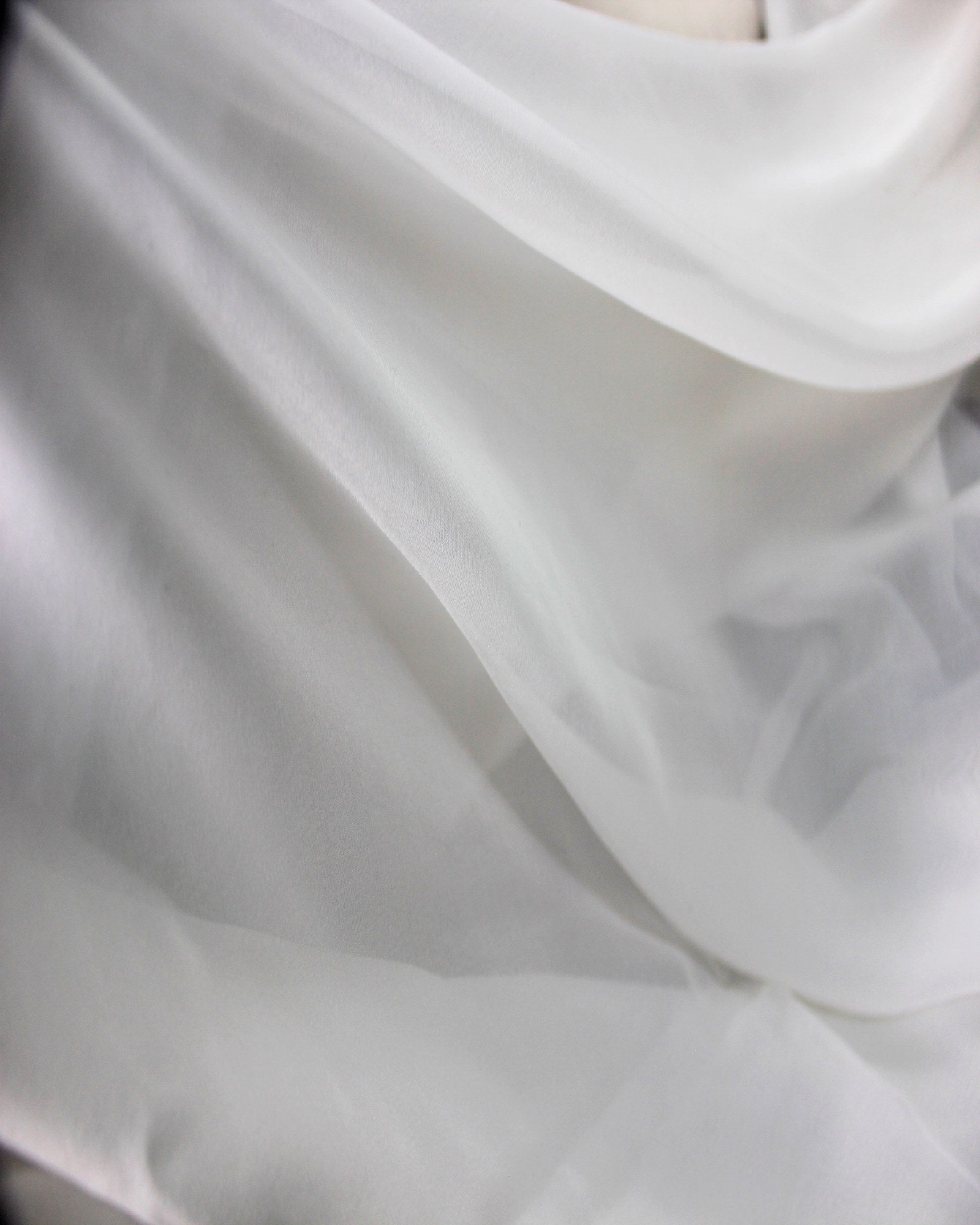 White 10 momme mulberry silk chiffon arranged in broad flowing folds, showing its lightweight movement and airy fluid drape.