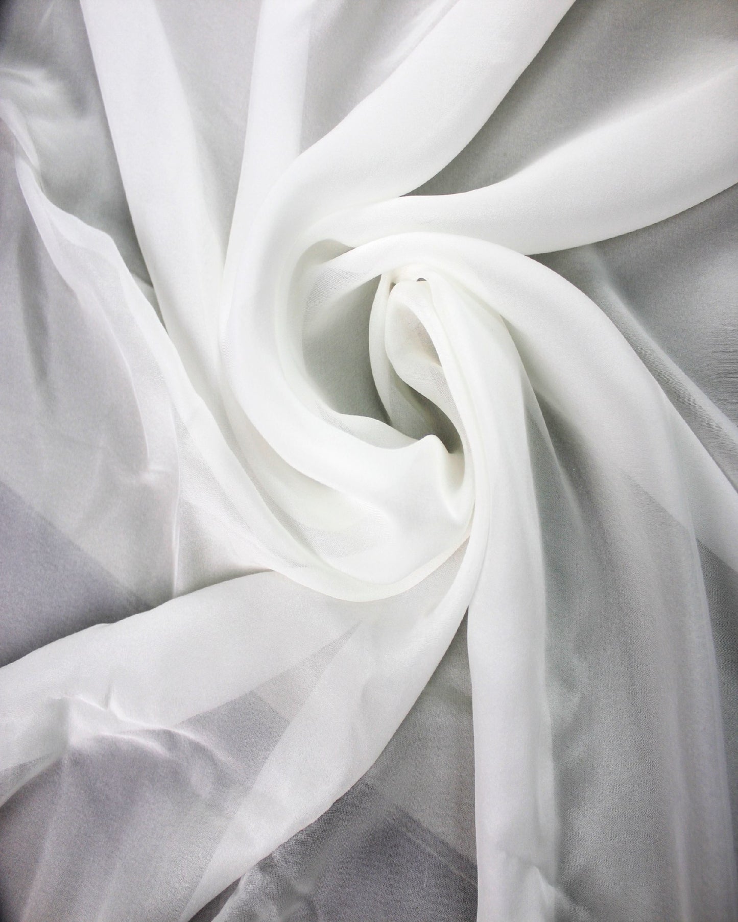 White 10 momme silk chiffon arranged in flowing swirled folds, showing its sheer lightweight structure and fluid drape.