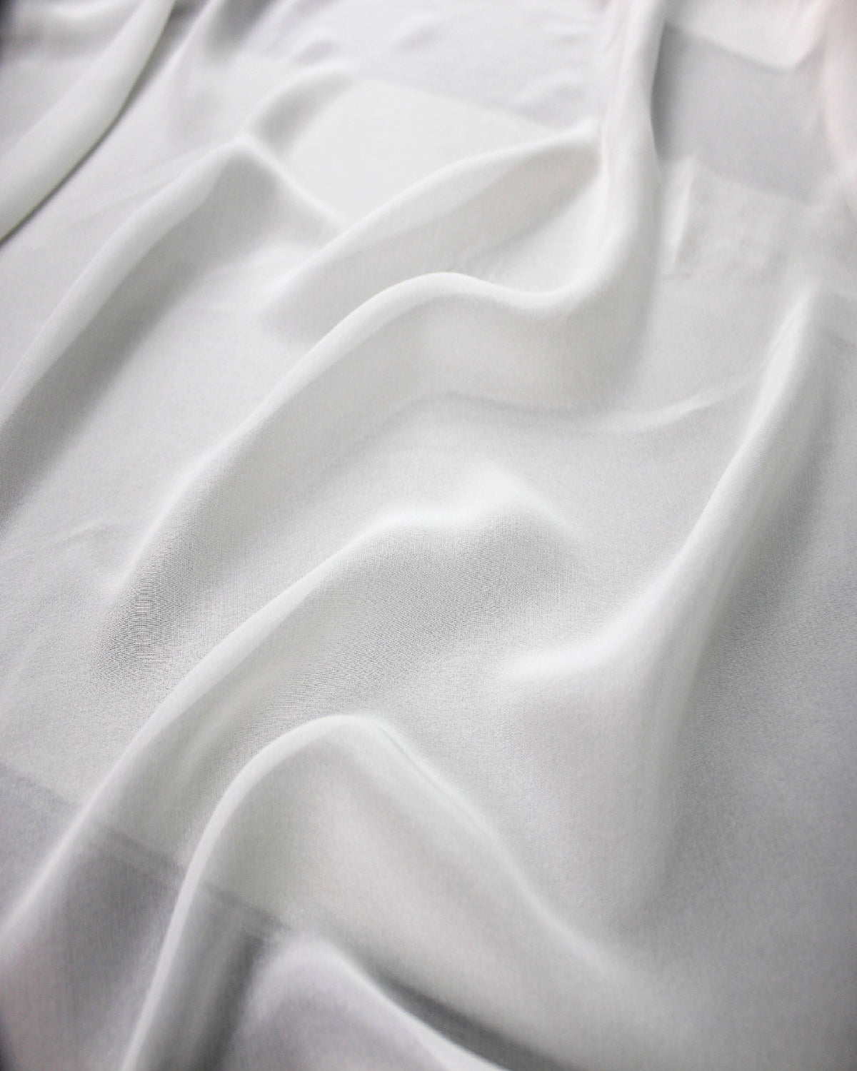 White 10 momme silk chiffon spread in natural folds, highlighting its soft fluid drape, airy body and subtle sheen.