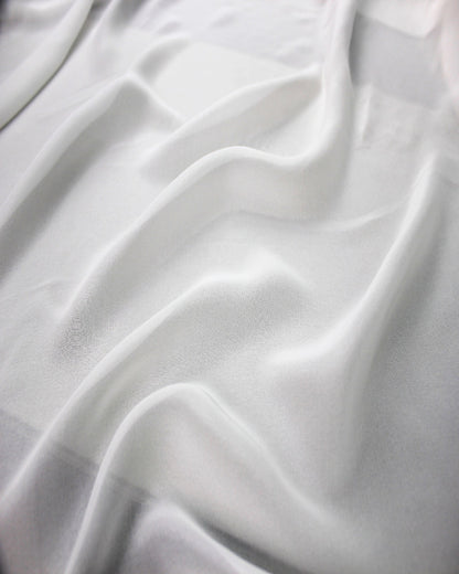 White 10 momme silk chiffon spread in natural folds, highlighting its soft fluid drape, airy body and subtle sheen.