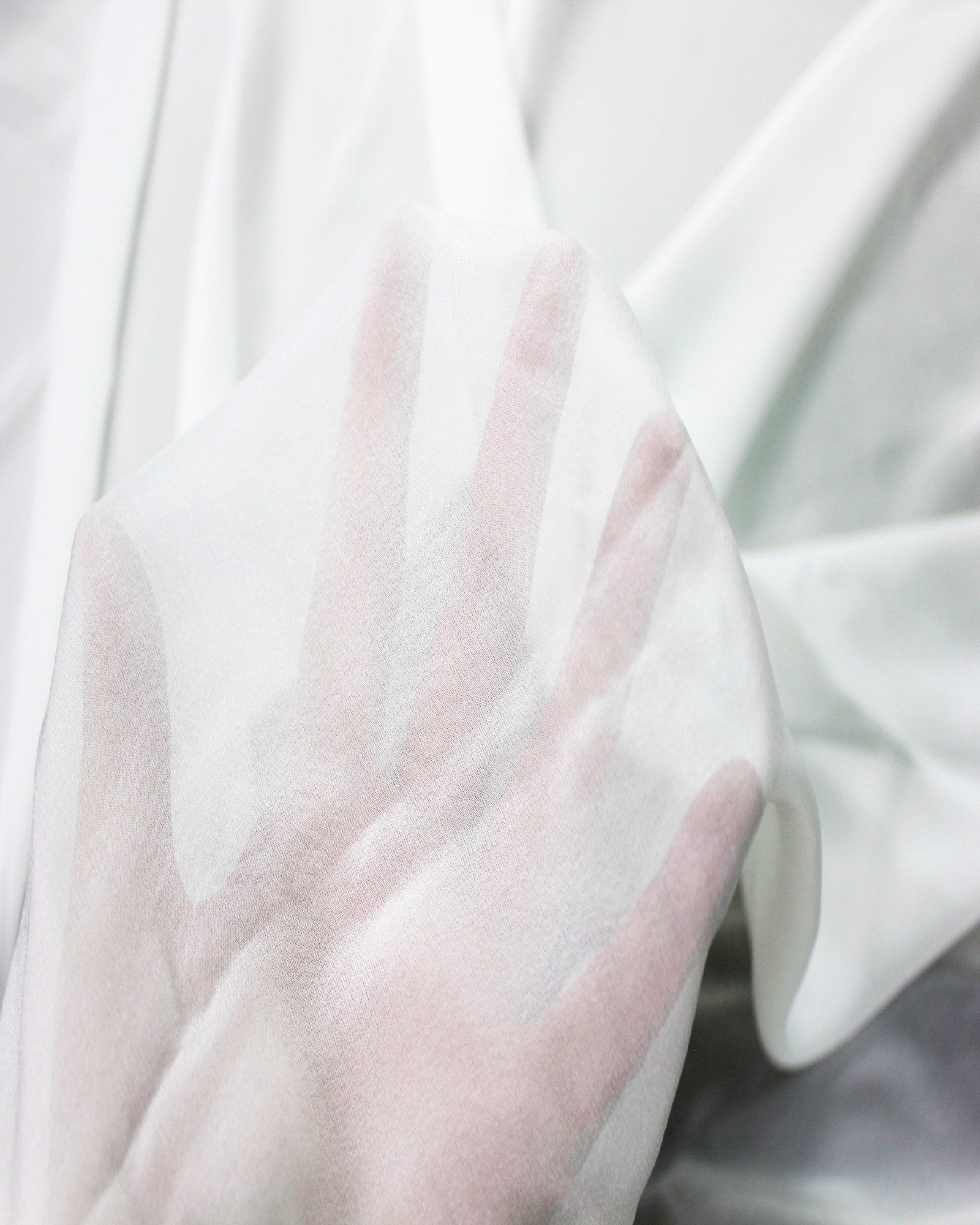 White 10 momme silk chiffon held over a hand to demonstrate its sheer transparency, fine weave and lightweight construction.