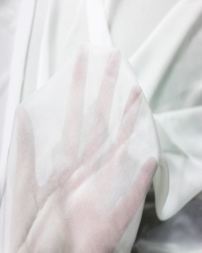 White 10 momme silk chiffon held over a hand to demonstrate its sheer transparency, fine weave and lightweight construction.