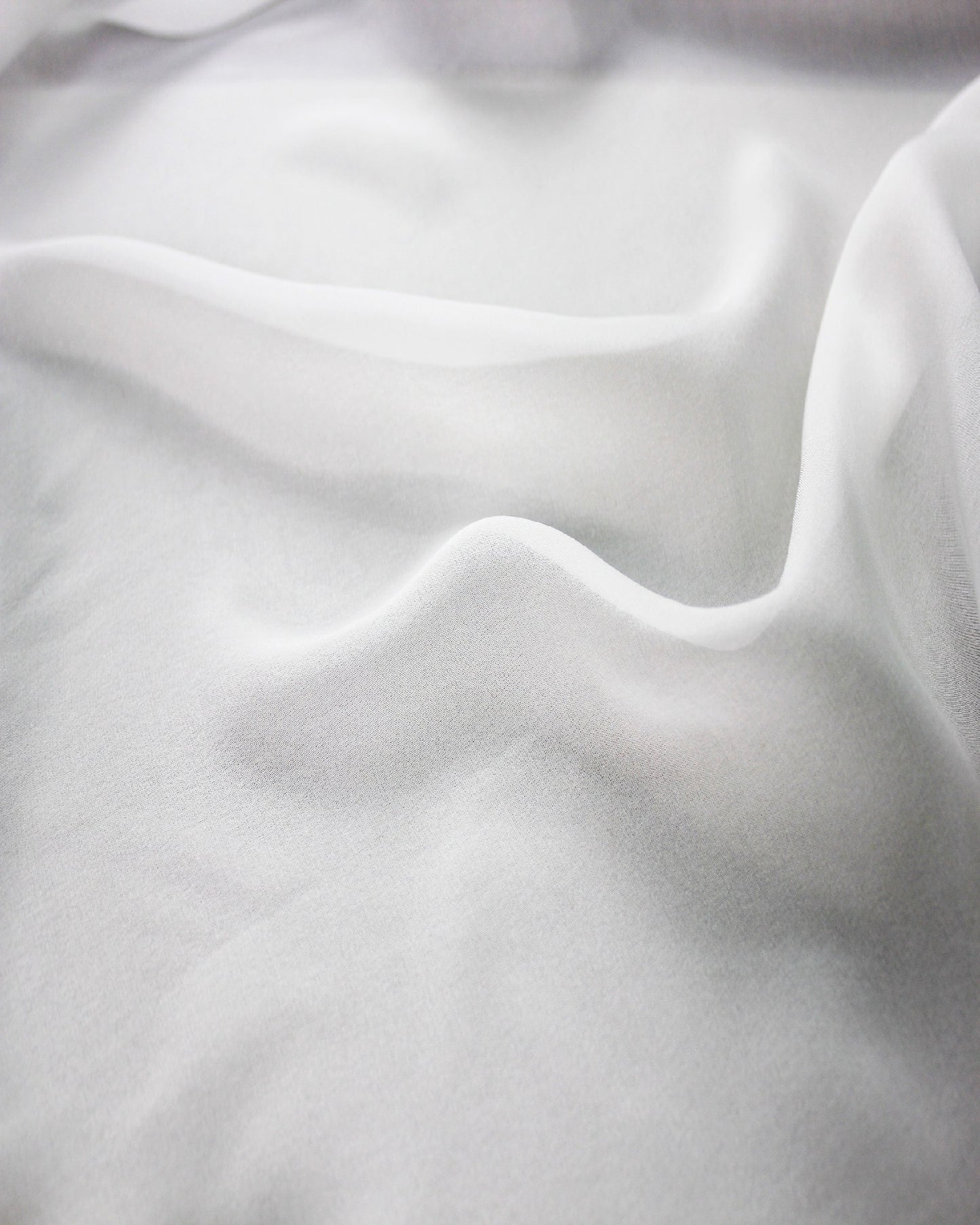 Close view of white 10 momme silk chiffon in soft waves, showing its fine woven surface, subtle lustre and airy drape.