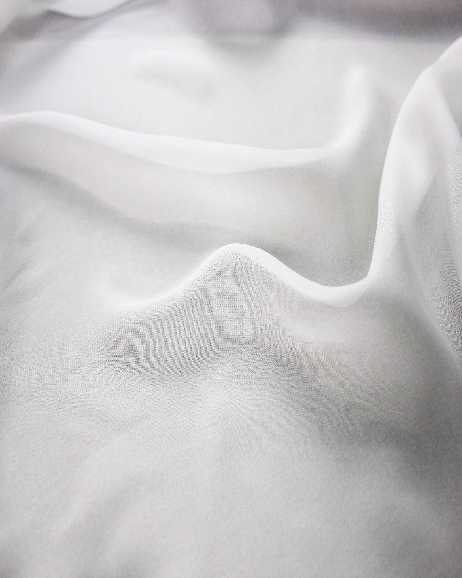 Close view of white 10 momme silk chiffon in soft waves, showing its fine woven surface, subtle lustre and airy drape.