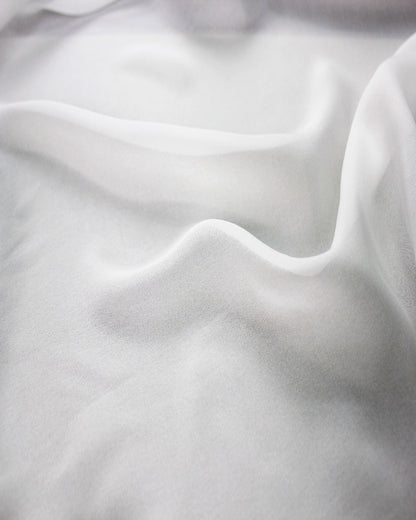 Close view of white 10 momme silk chiffon in soft waves, showing its fine woven surface, subtle lustre and airy drape.