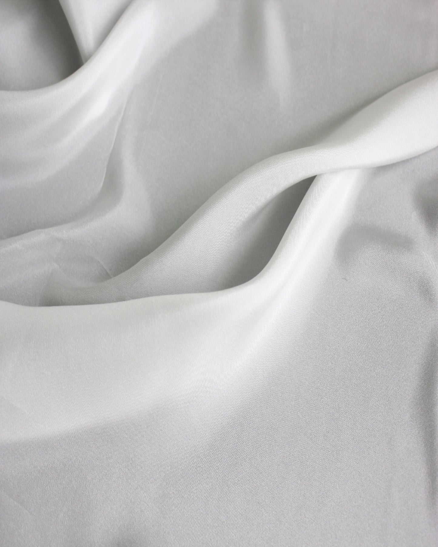 White 12 momme silk Habotai spread in broad natural waves, showing its smooth surface and flowing lightweight drape.