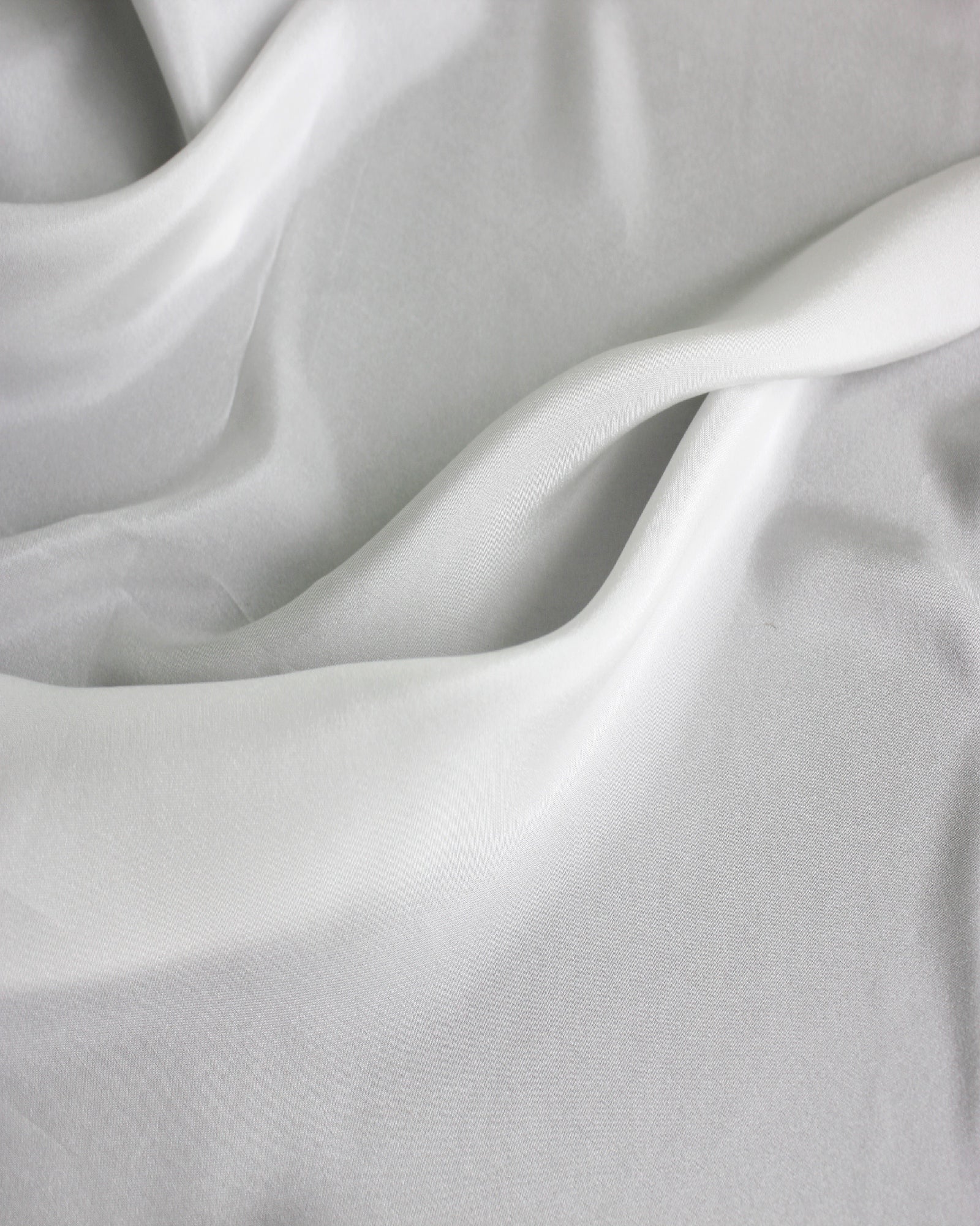 White 12 momme silk Habotai spread in broad natural waves, showing its smooth surface and flowing lightweight drape.