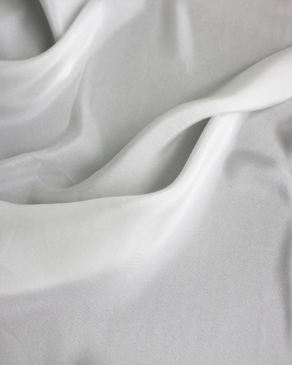 White 12 momme silk Habotai spread in broad natural waves, showing its smooth surface and flowing lightweight drape.