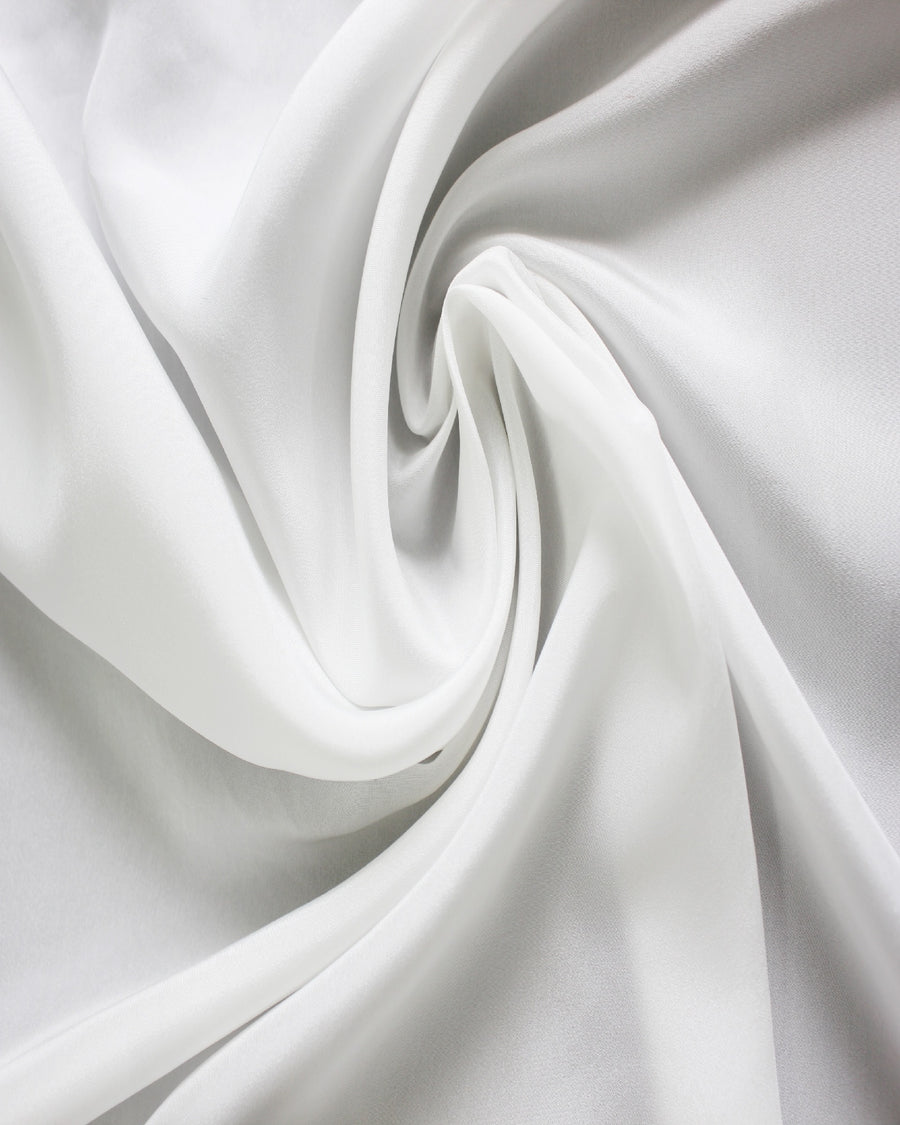 White 12 momme silk Habotai fabric arranged in flowing folds, showing its smooth surface, soft sheen and fluid drape.