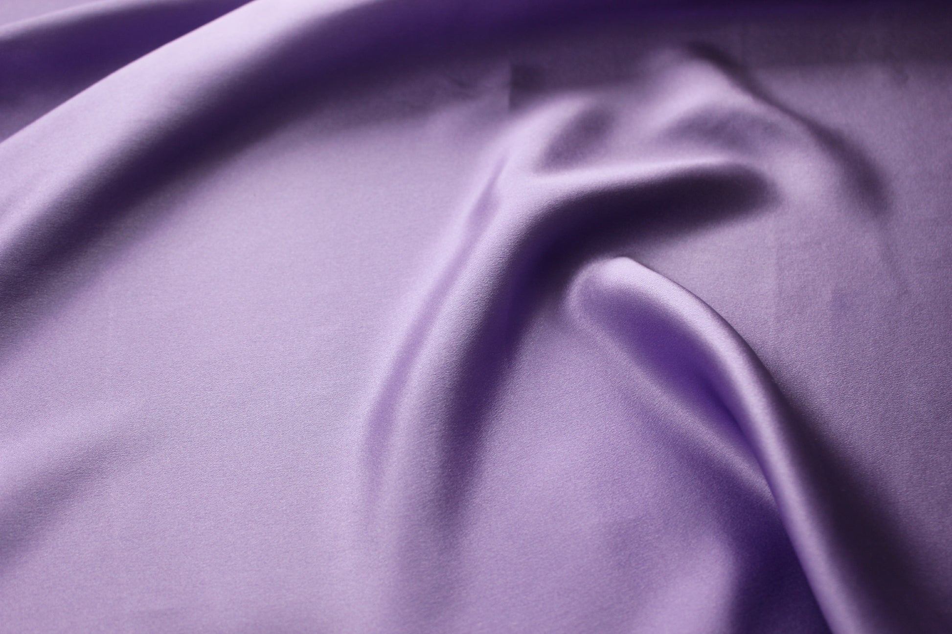 Close-up of lavender silk charmeuse showing a smooth satin face, fine surface texture and pearlescent lustre.