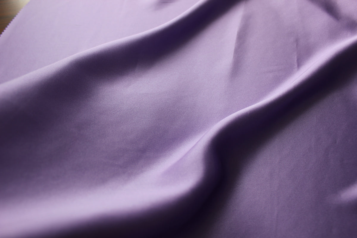 Lavender silk charmeuse fabric with a smooth surface, soft sheen and long flowing folds.